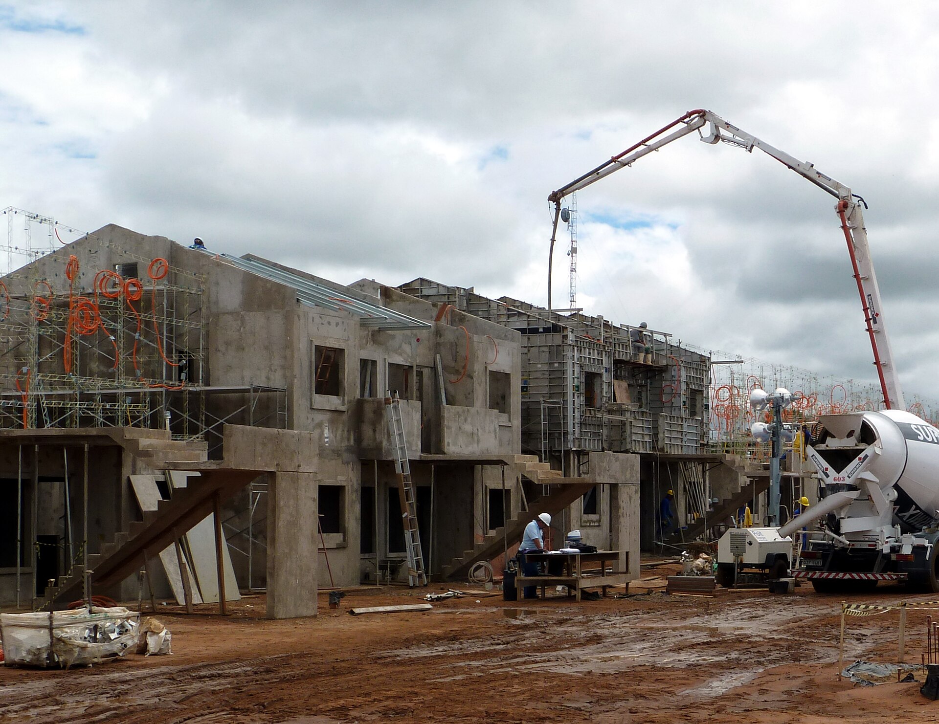 Casas de concreto em construção em Campo Grande, com bomba de concreto e um técnico conferindo papéis numa mesa no canteiro