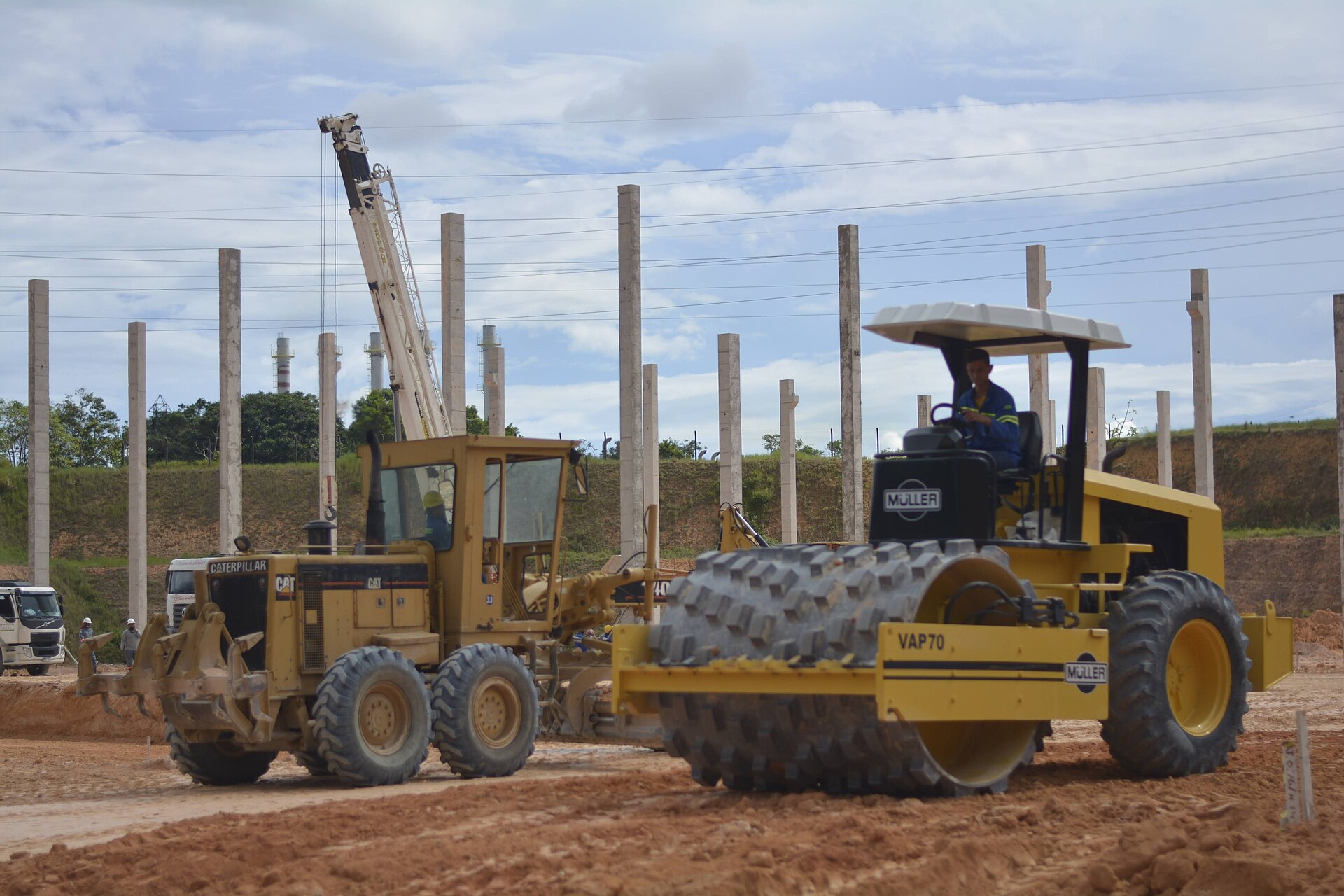 Motoniveladora e rolo compactador preparando o terreno entre pilares de concreto em Manaus